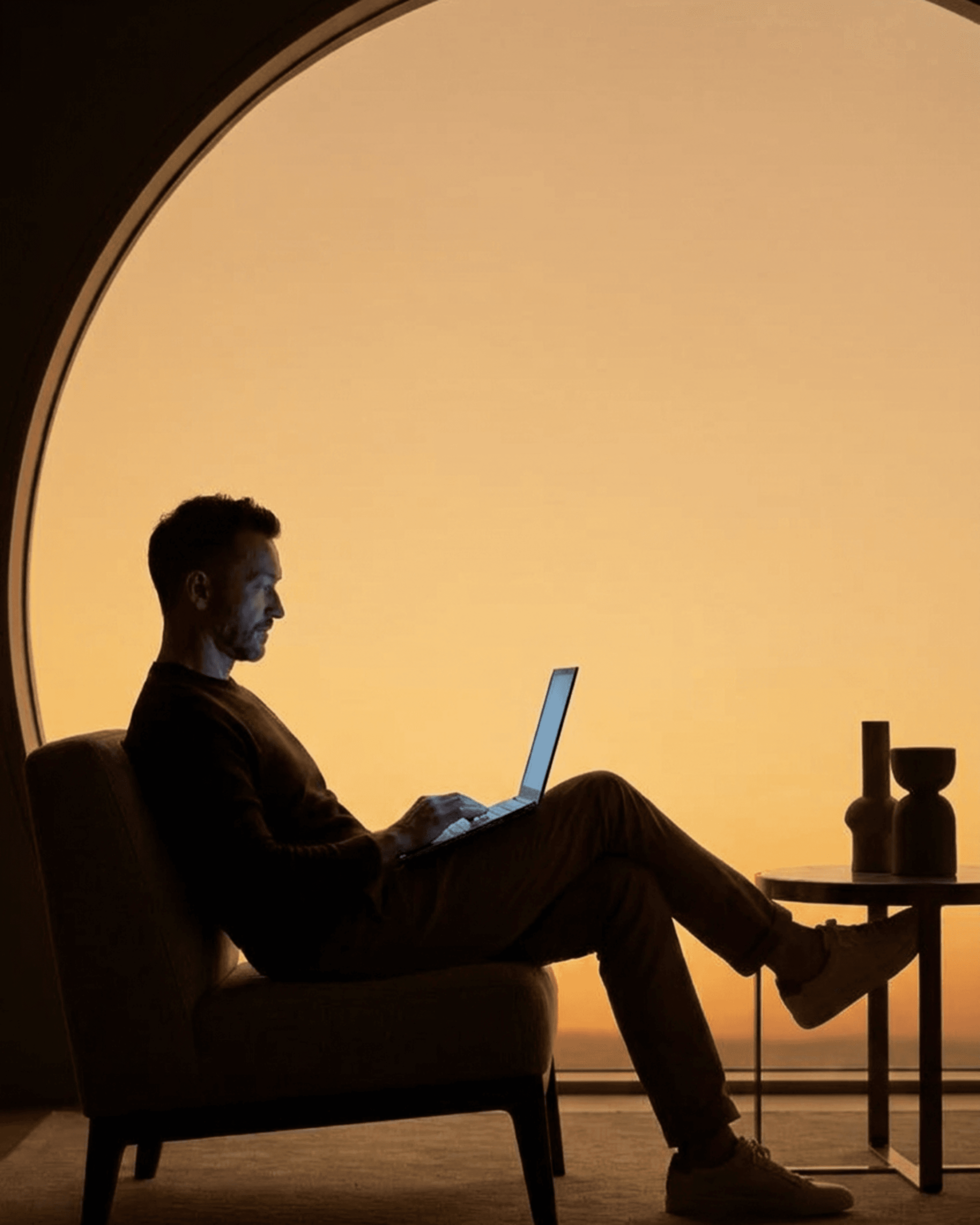Founder working on a laptop framed by an arched window at sunset
